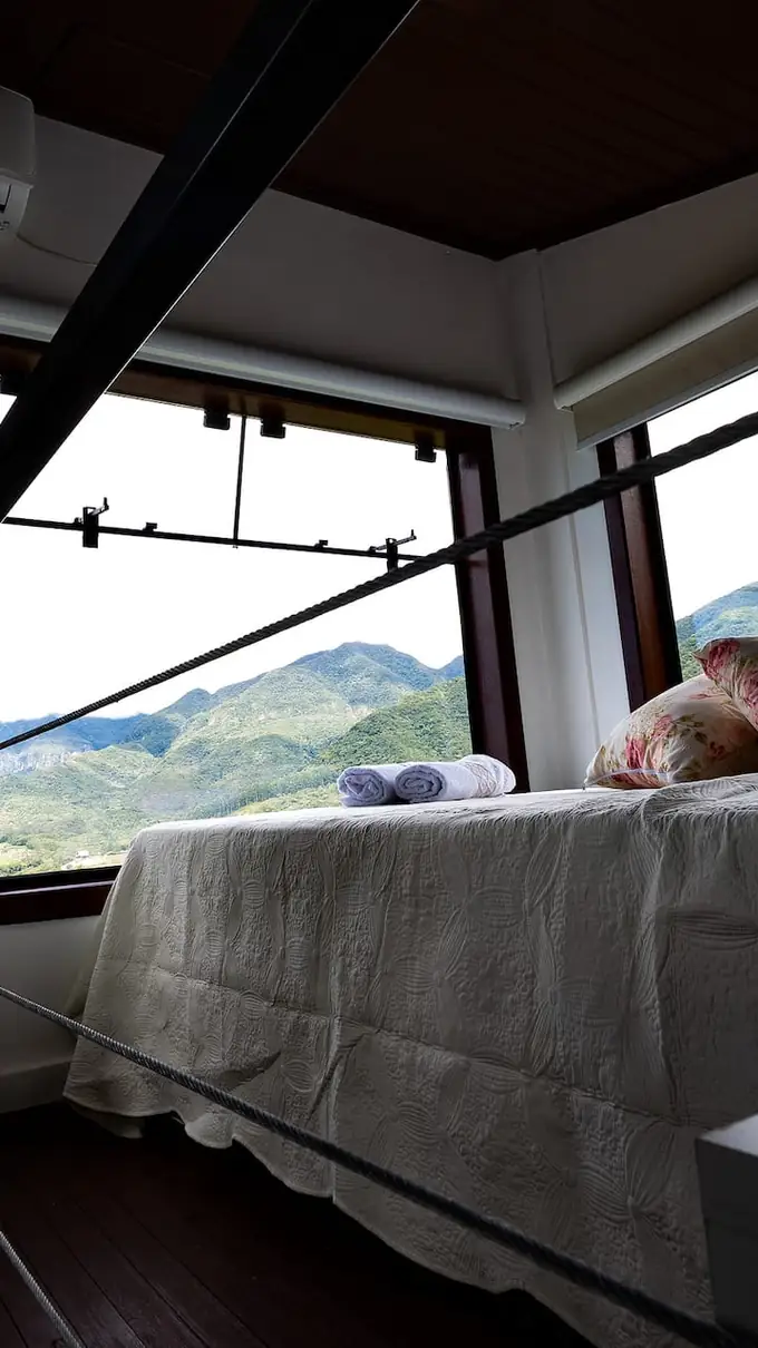 Cama de casal no mezanino, de frente para a janela ampla e o vale