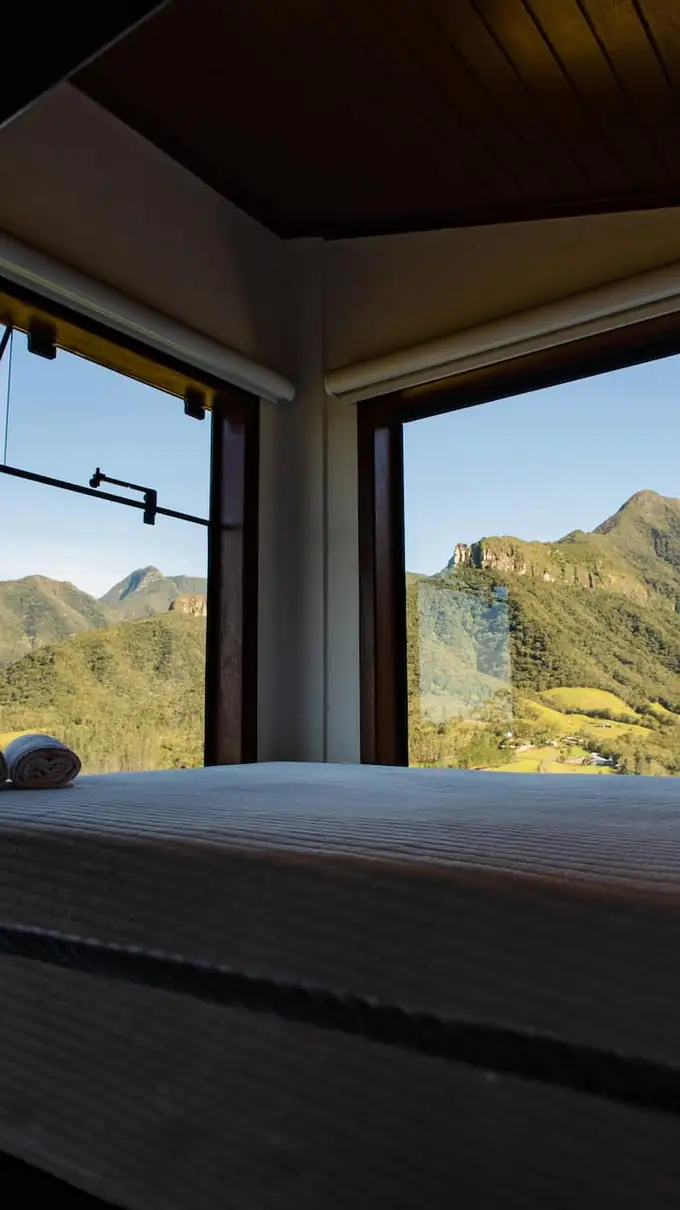 Cama de casal diante da janela ampla com vista para as montanhas