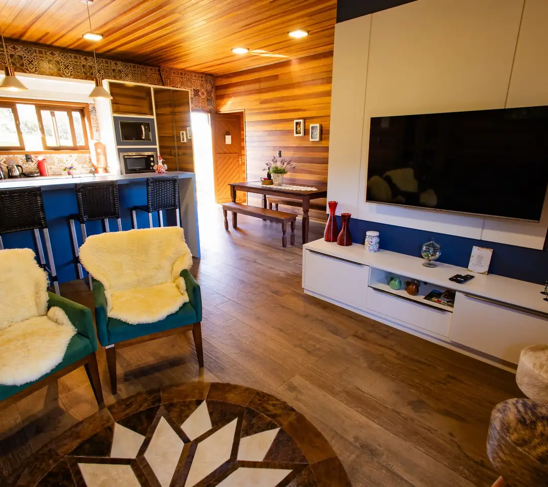 Sala do chalé com sofá, poltronas e TV na parede de madeira