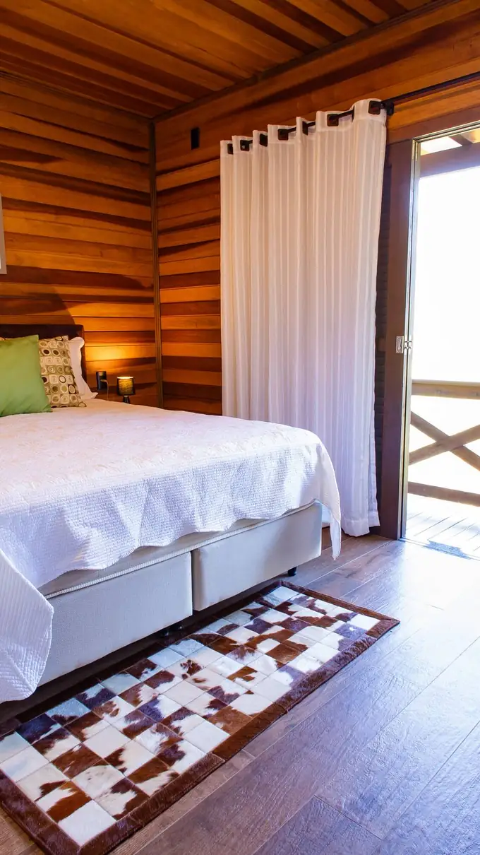 Quarto com cama queen, roupa de cama branca e janela para o vale