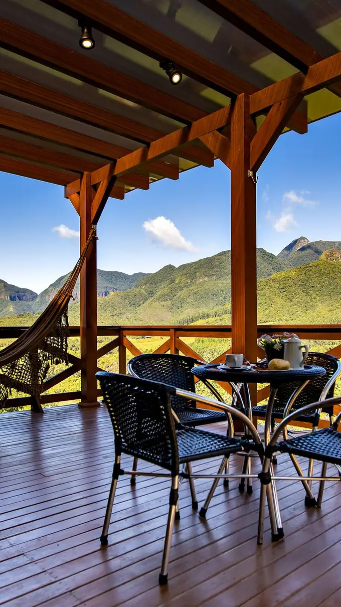 Varanda de madeira com rede, mesa e as montanhas ao fundo