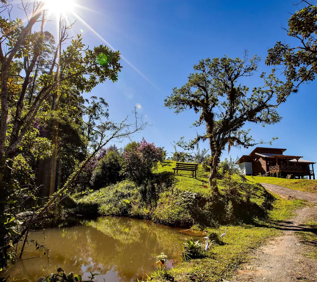 Açude e caminho de terra dentro da propriedade, com o chalé ao alto